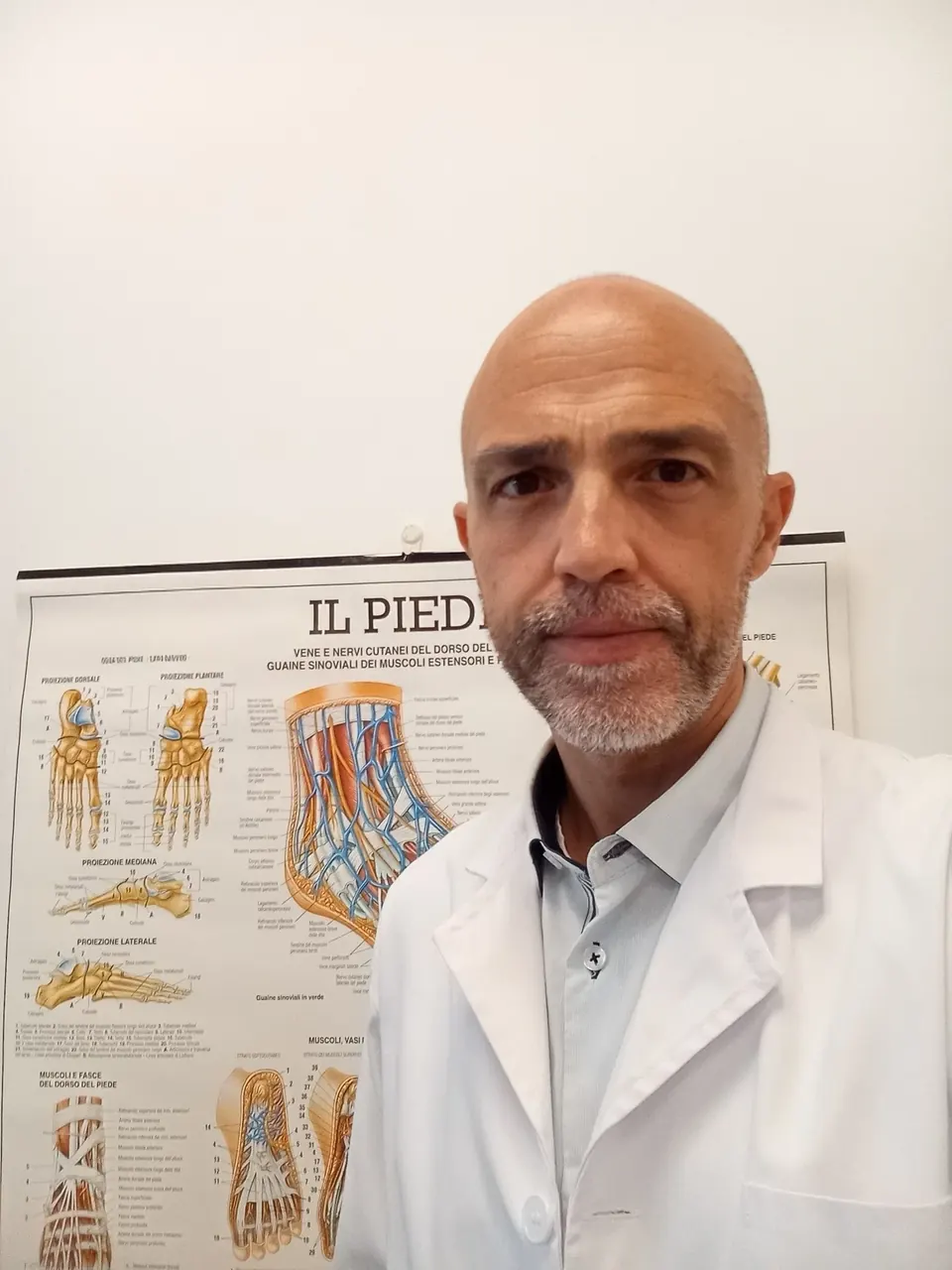 Daniel Michieletto in camice bianco davanti al poster anatomico del piede